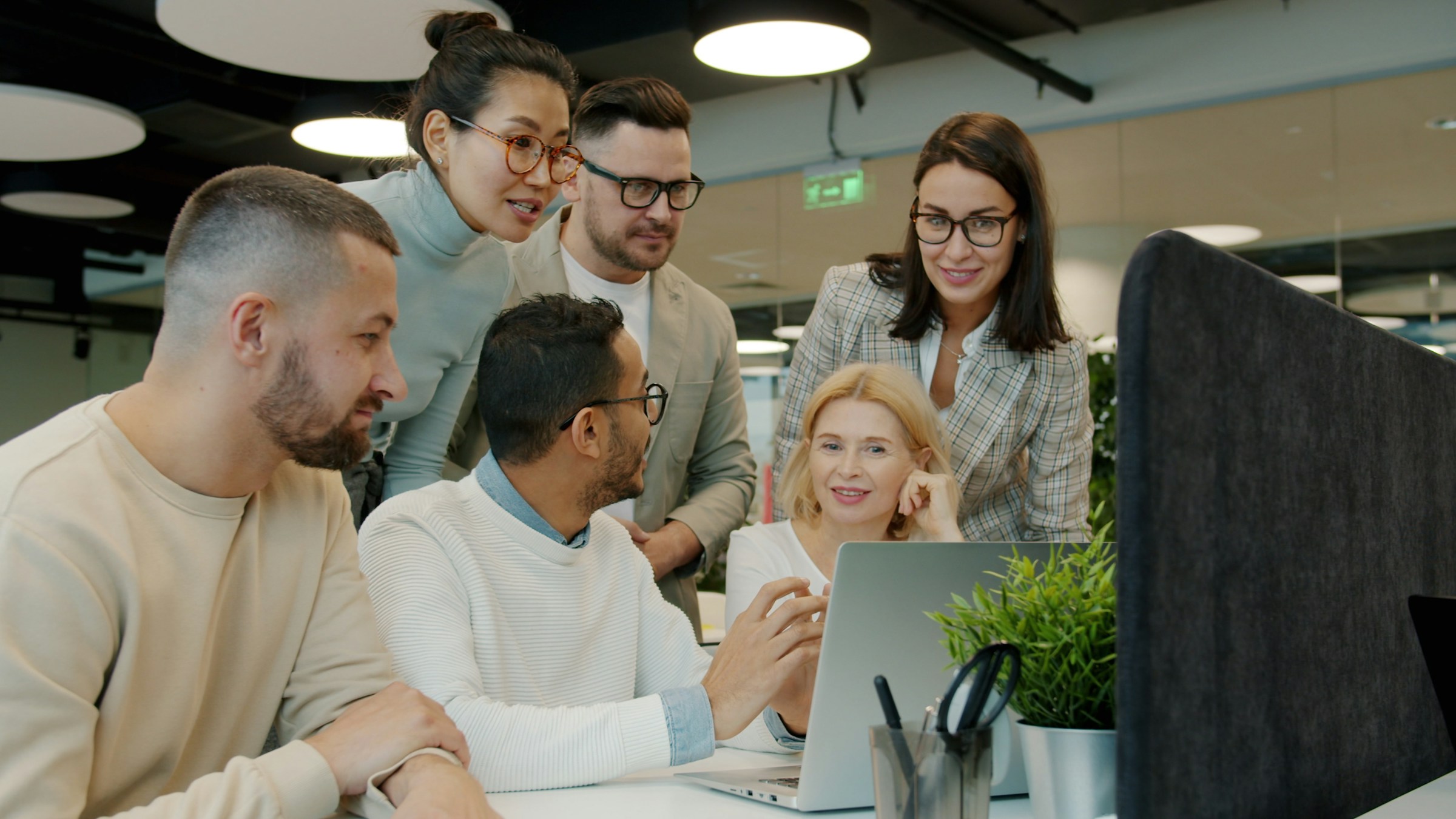 A diverse delivery team collaborating around laptops and a shared screen
